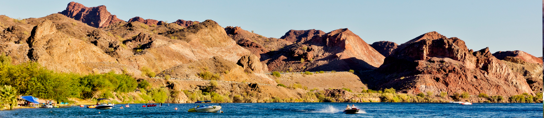 The Colorado River is alive with action as multiple boats navigate the river at the base of barren desert mountains.
