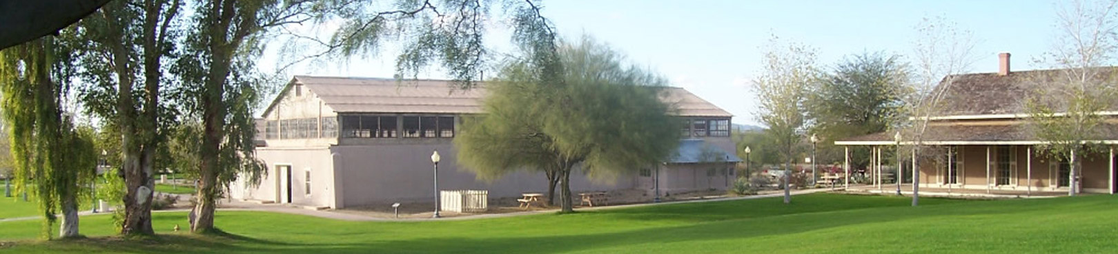 Two park buildings sit amid shade trees on the far end of a field of green grass.