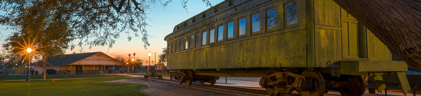A historic yellow train car that shows sign of wear sits in the main yard at sunset.