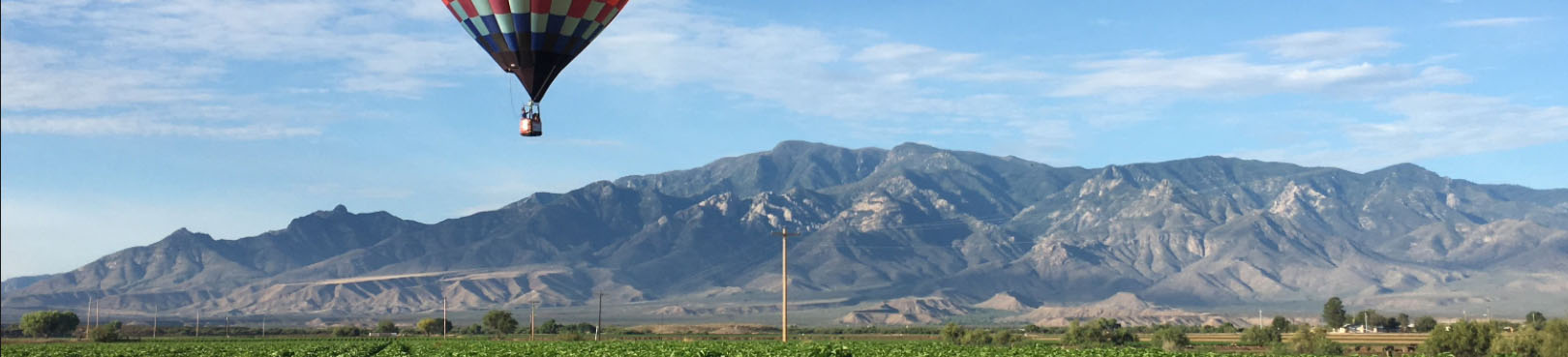 People in a hot air balloon enjoy panoramic views of Mt. Graham towering in the distance below partly clouds blue skies.