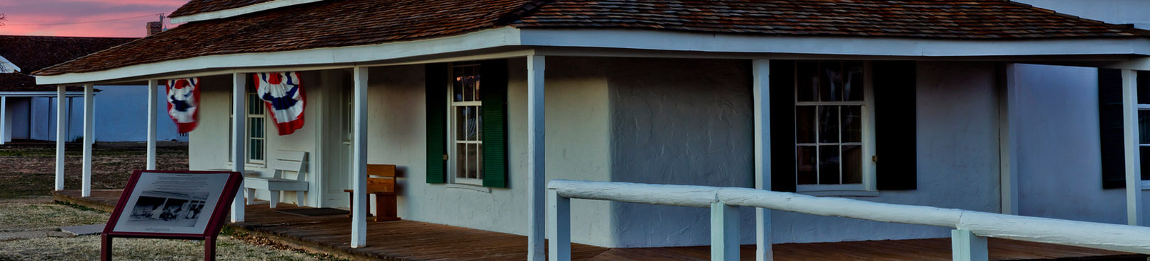 One of the original buildings that housed Army personnel is pictured at sunset and decorated with red, white, and blue banners..
