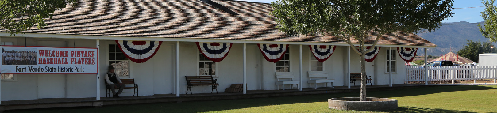 A man sits on a bench in front of a historic building at the park adorned with festive red, white, and blue banners.