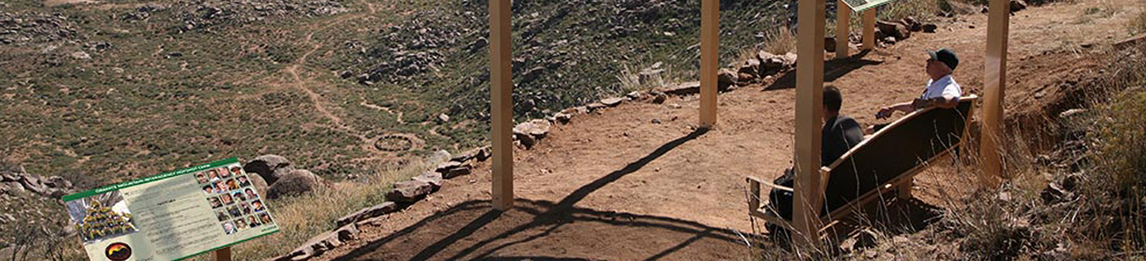 Hikers take a break on a bench at an interpretive site along the trail to the fatality site which can be seen in the desert below.