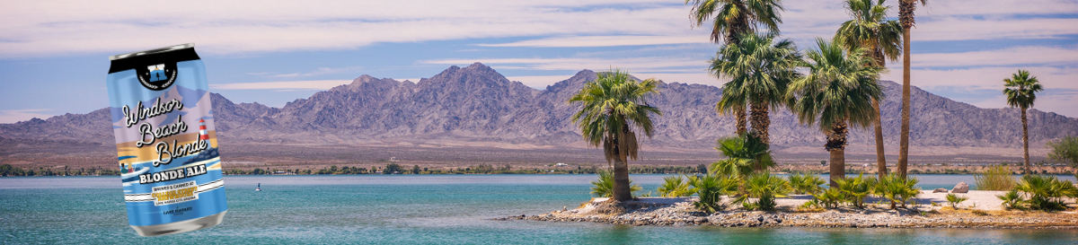 A photo of the greenish blue lake with a white sand beach and palm trees and mountains in the distance. A can of the Windsor Beach Blonde beer is overlaid on the photo.